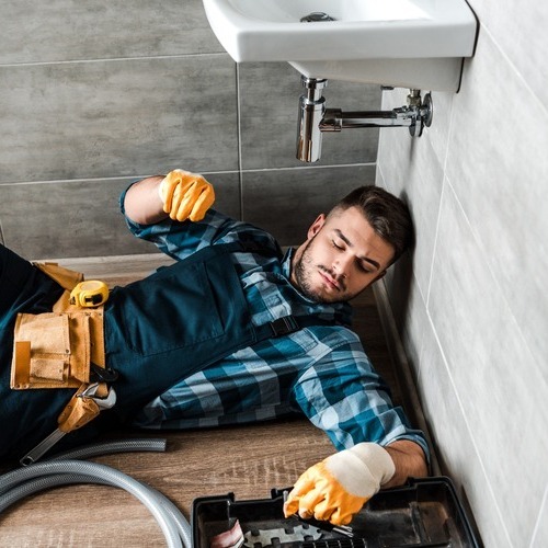 A man laying on the ground in front of a sink.