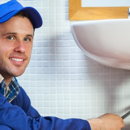 A man in blue shirt holding pipe near sink.