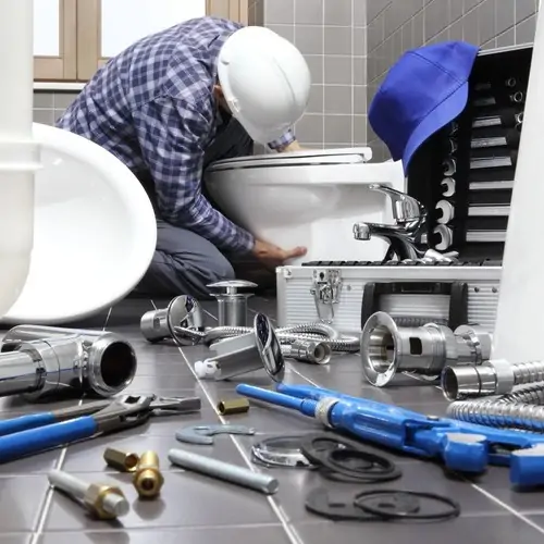 A man working on the toilet in his bathroom.